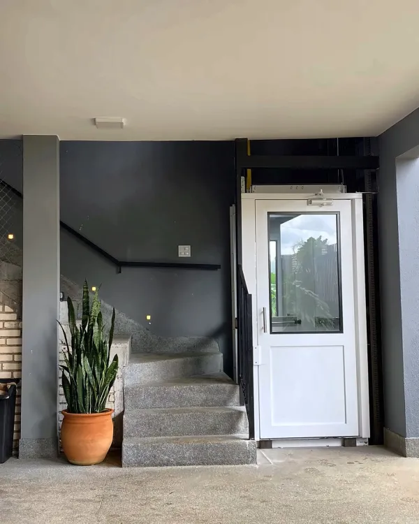 Elevador com porta branca ao lado da escada em área coberta