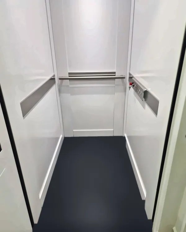 Interior da cabine com painéis brancos, corrimão em inox e piso azul-marinho