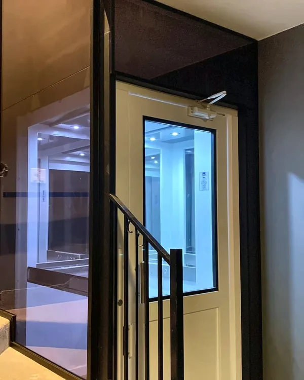 Caixa do elevador em vidro iluminada à noite, ao lado da escada